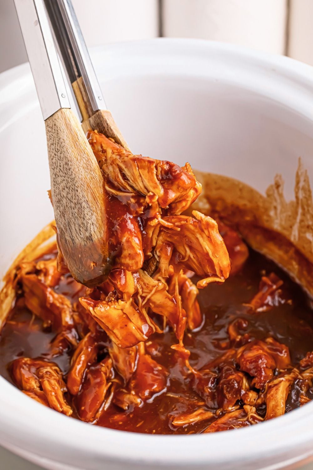 Crockpot Apple Butter BBQ Pulled Chicken being lifted up out of crockpot with tongs