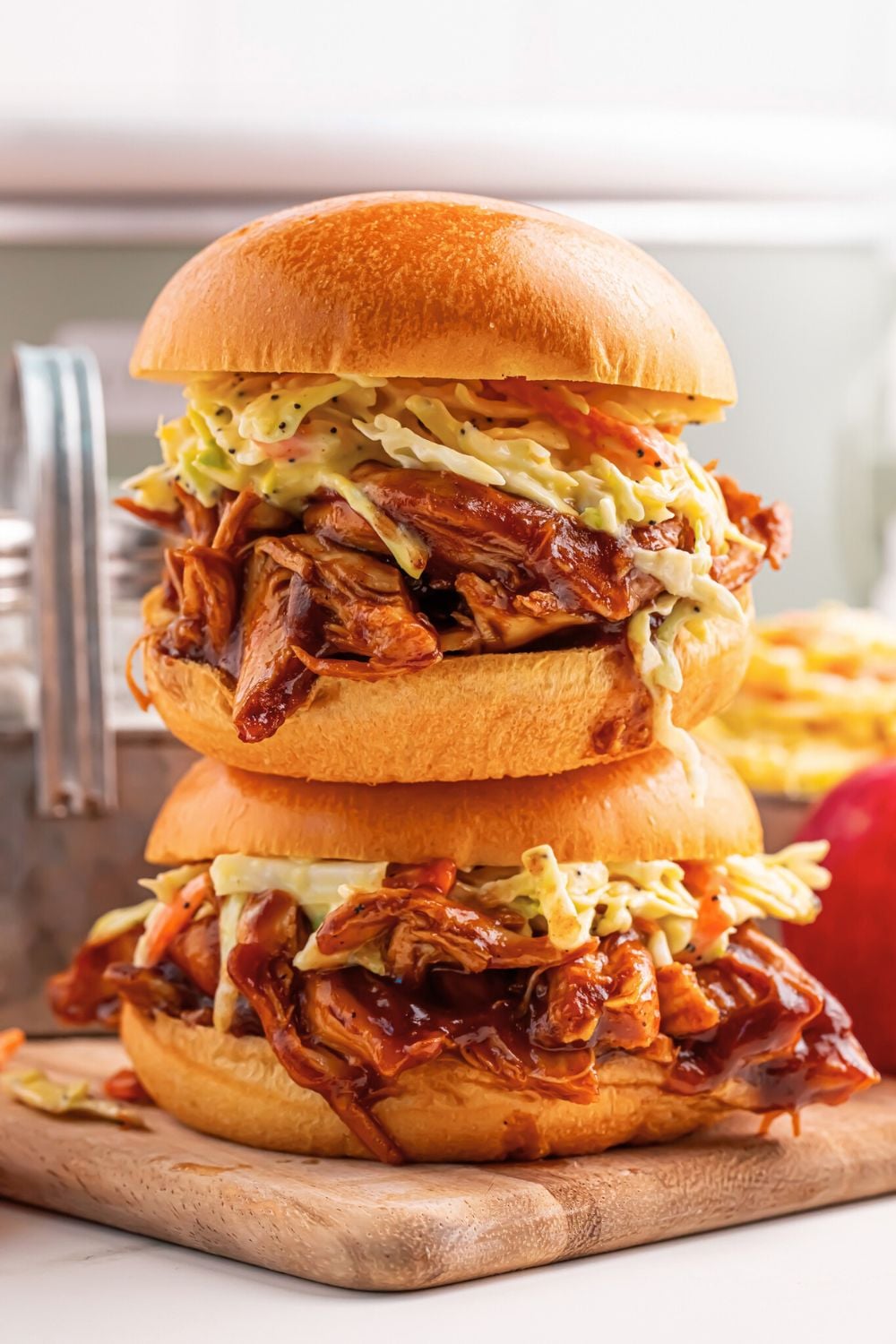 Crockpot Apple Butter BBQ Pulled Chicken sandwiches stacked on a cutting board with a crockpot behind it and tomatoes to side