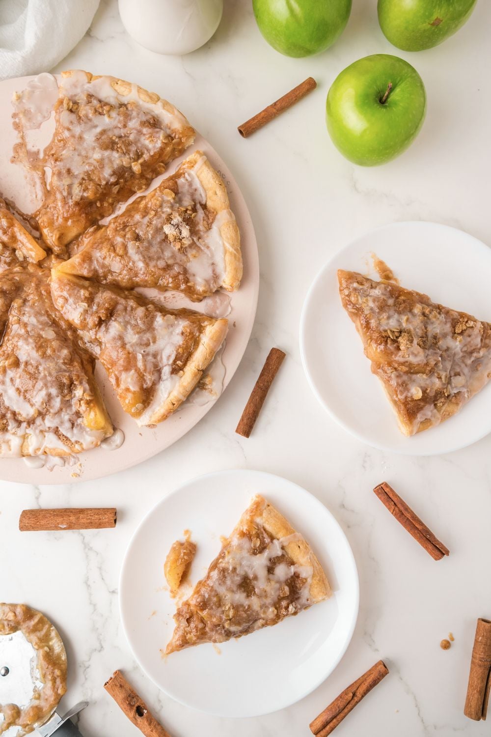 overhead look of table with Apple Pie Pizza and plates with slices of pizza on it and cinnamon sticks around table