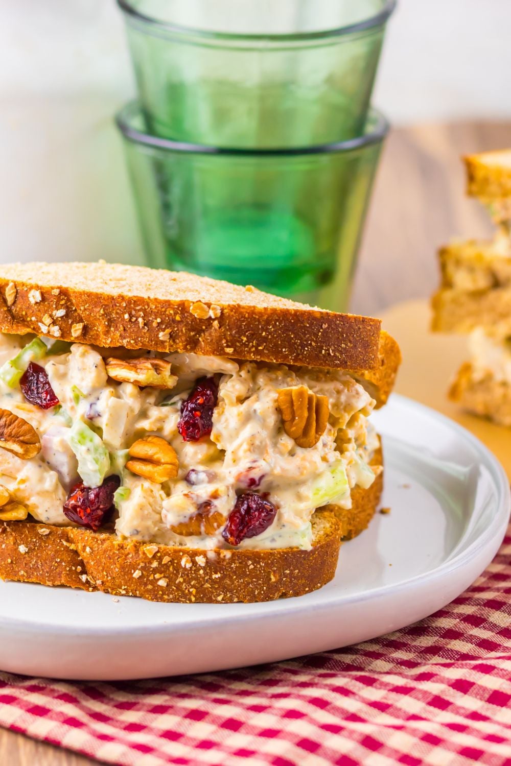 Thanksgiving Turkey Salad sandwich on white plate sitting on table with green glasses behind it on table 