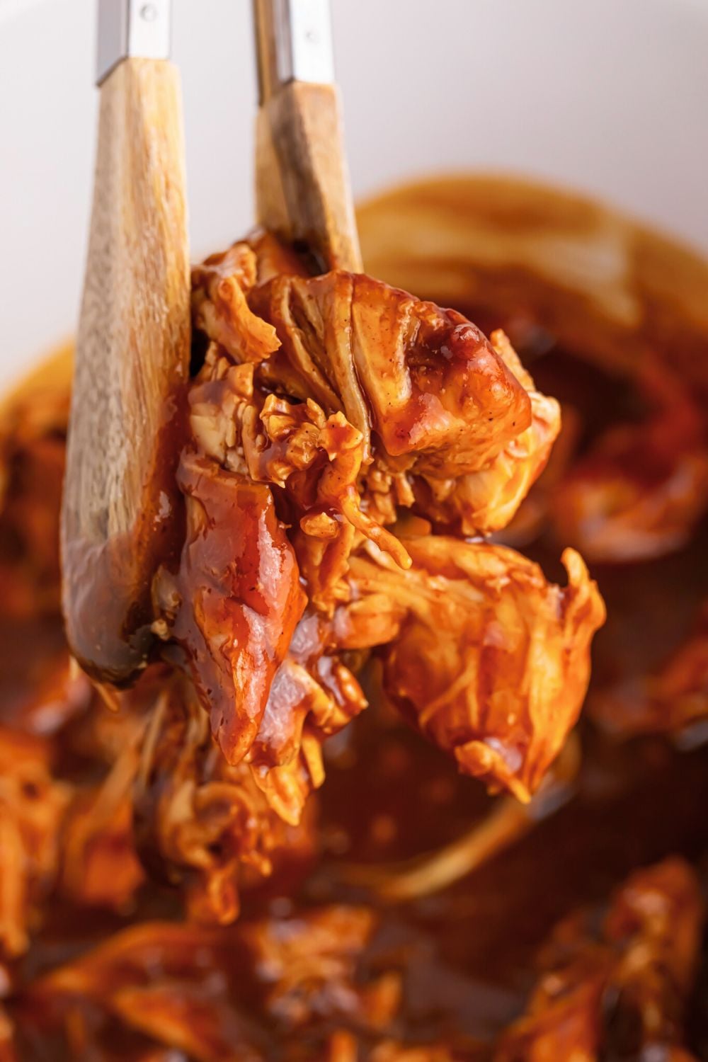 Crockpot Apple Butter BBQ Pulled Chicken in crockpot being lifted out of crockpot with tongs