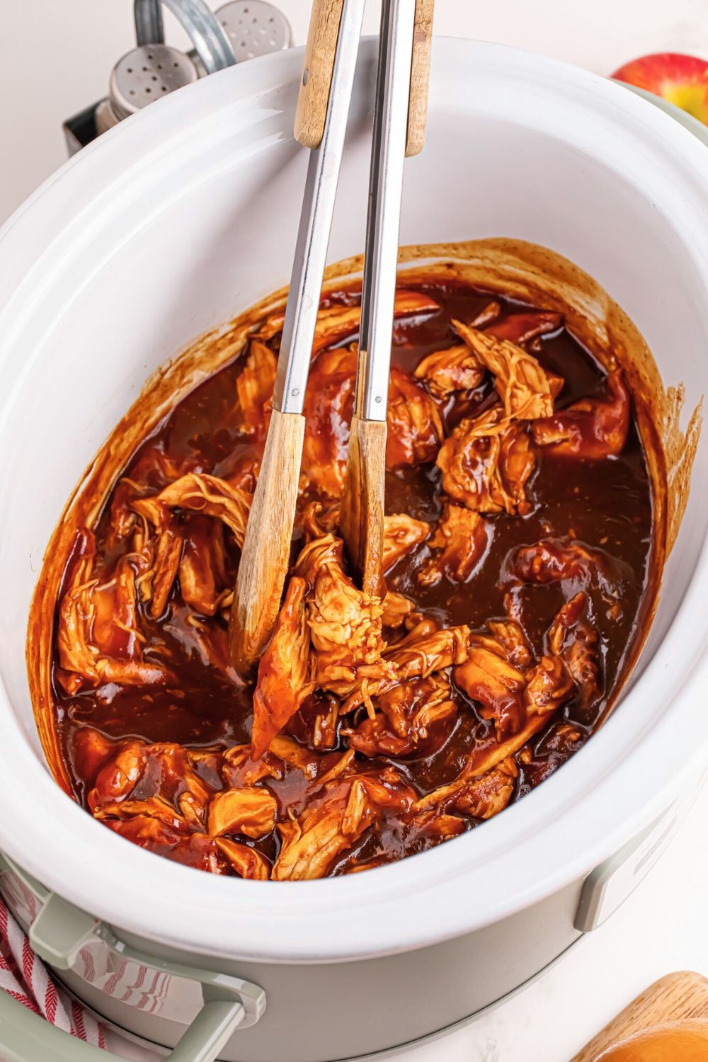 look of Crockpot Apple Butter BBQ Pulled Chicken in crockpot with tongs sitting on side
