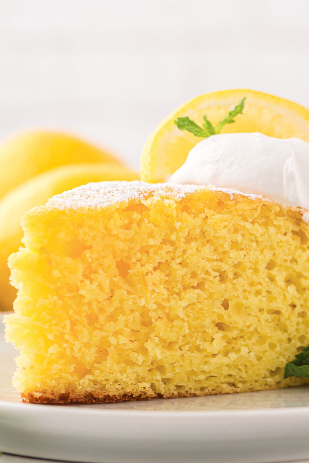 Italian Lemon Ricotta Cake sliced on plate with a dollop of whipped cream on top and a fresh lemon slice 