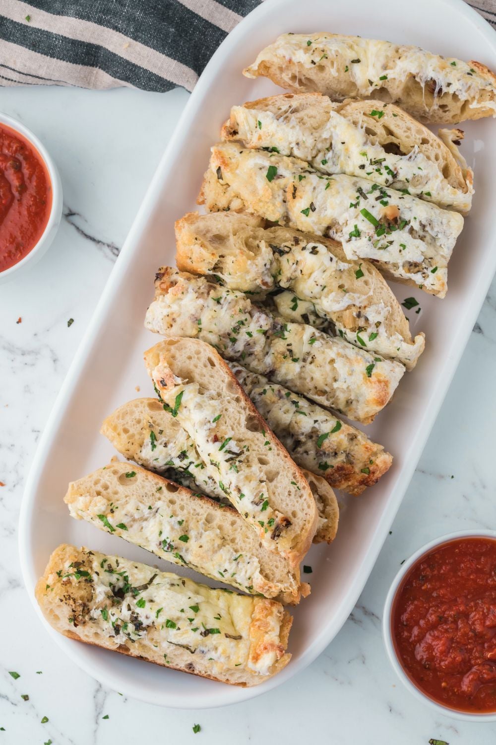 long platter with Cheesy Garlic Bread placed on it with two bowls of marinara sitting on each side of platter