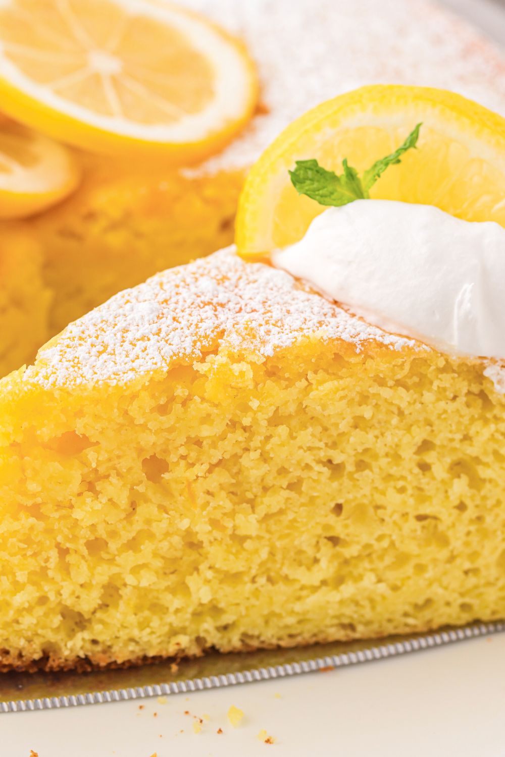 close up of Italian Lemon Ricotta Cake on plate with lemons sliced behind it on table 