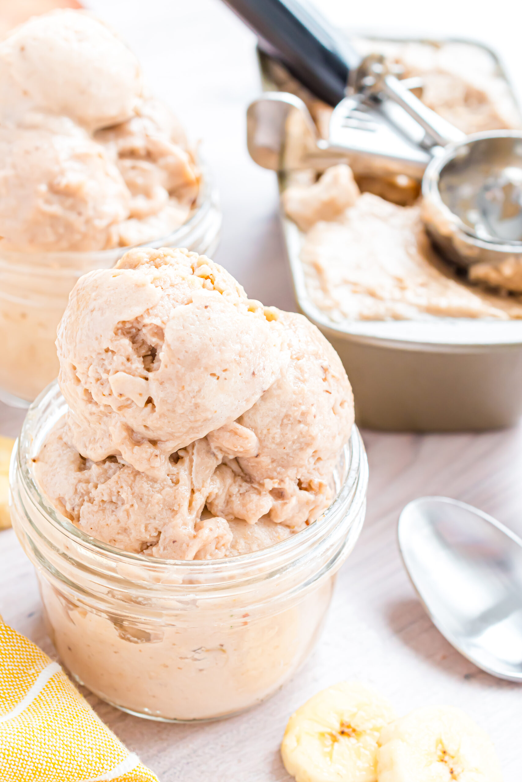 Banana Ice Cream in a glass bowl on table with slices of bananas around table 