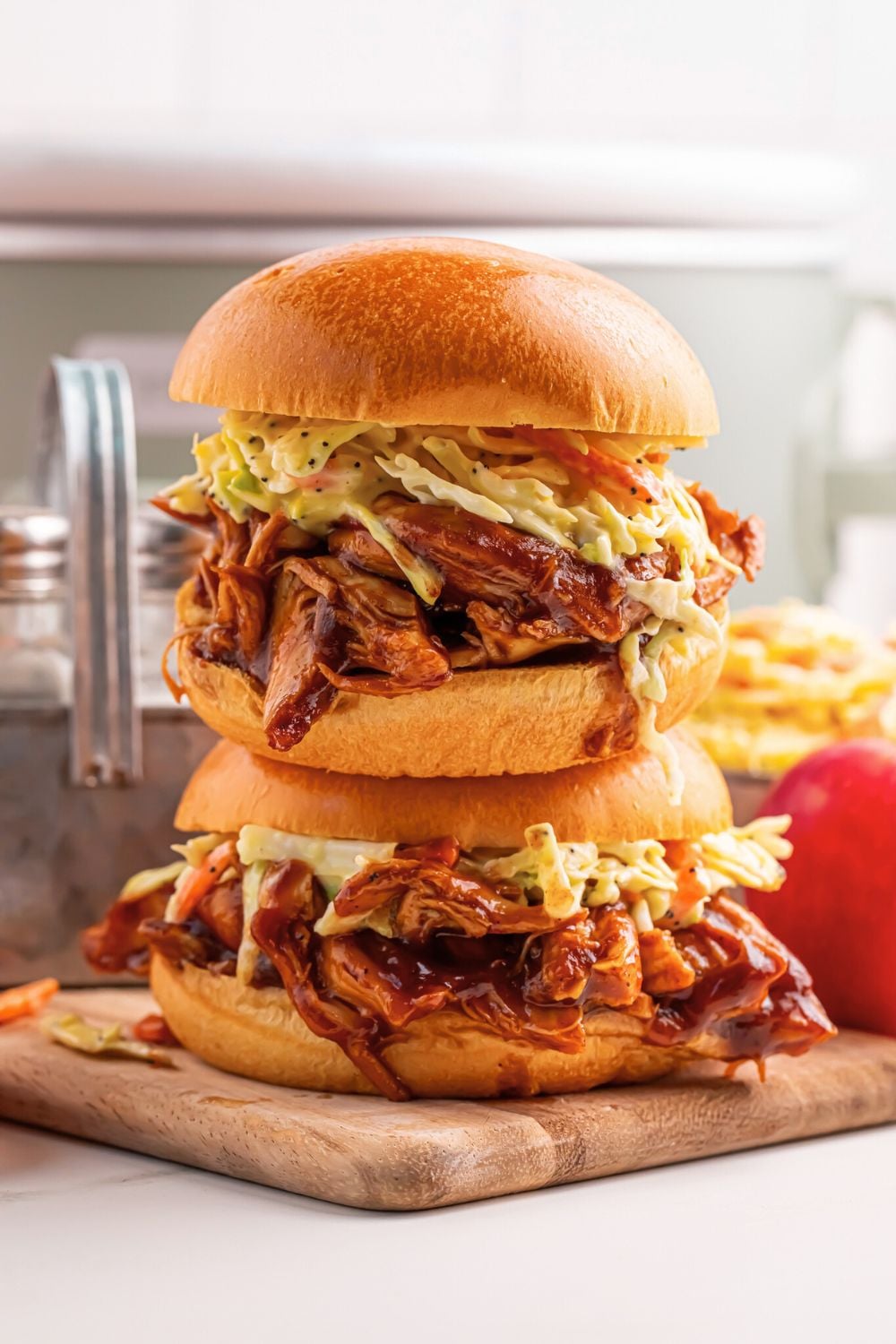 Crockpot Apple Butter BBQ Pulled Chicken sandwiches stacked on top of one another on table with crockpot behind it