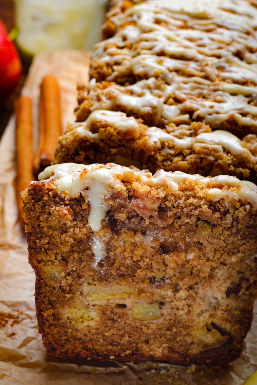 side view of the apple loaf cake on table with a sweet drizzle on top and two cinnamon sticks to the side on wooden table