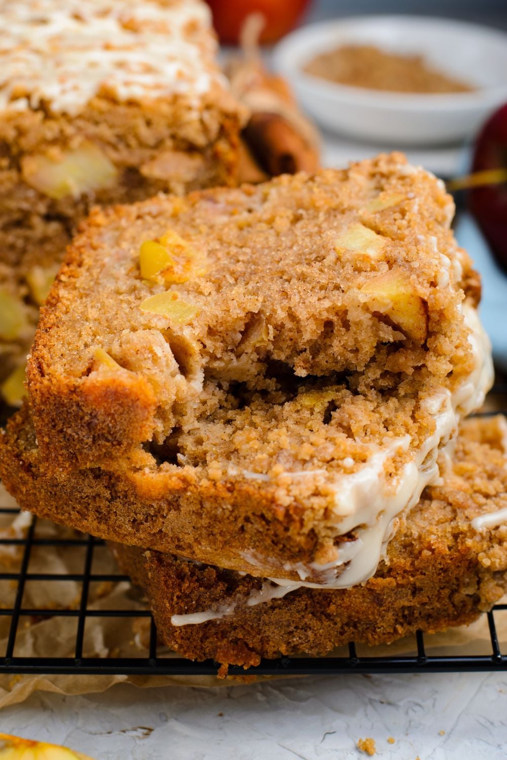 3 slices of Apple Cinnamon Loaf Cake on top of one another sitting on a wire cooling rack on table with the top slice having a few bites taken out of it