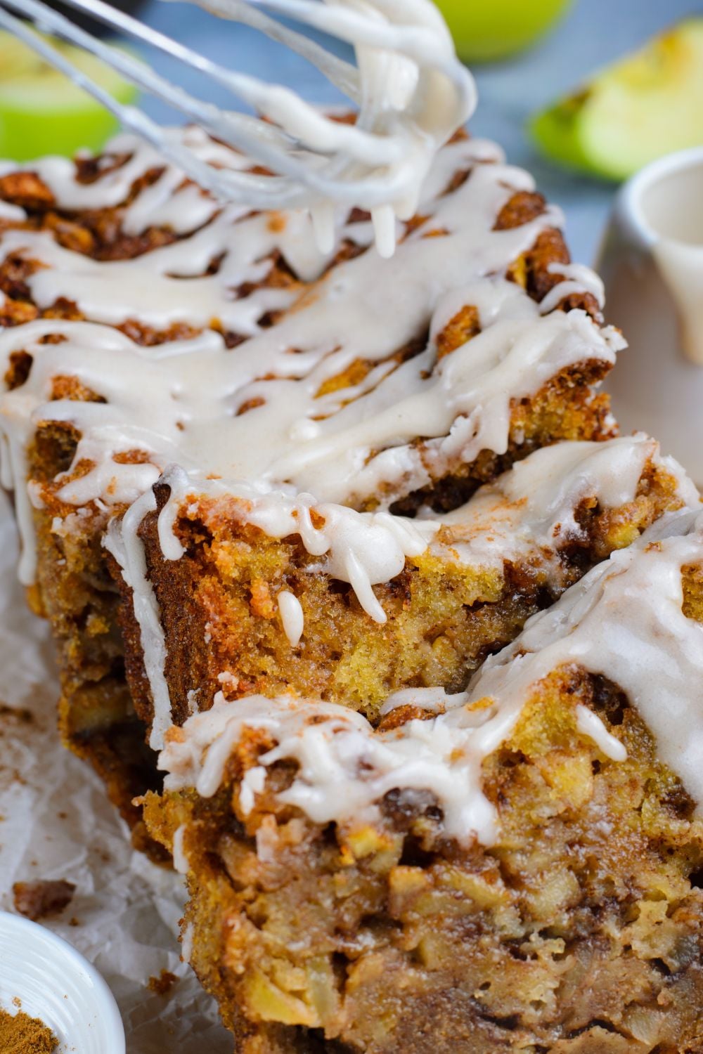 Amish Apple Fritter Bread sliced and placed on table spread out a bit with a whisk with glaze in background and green apples for decor