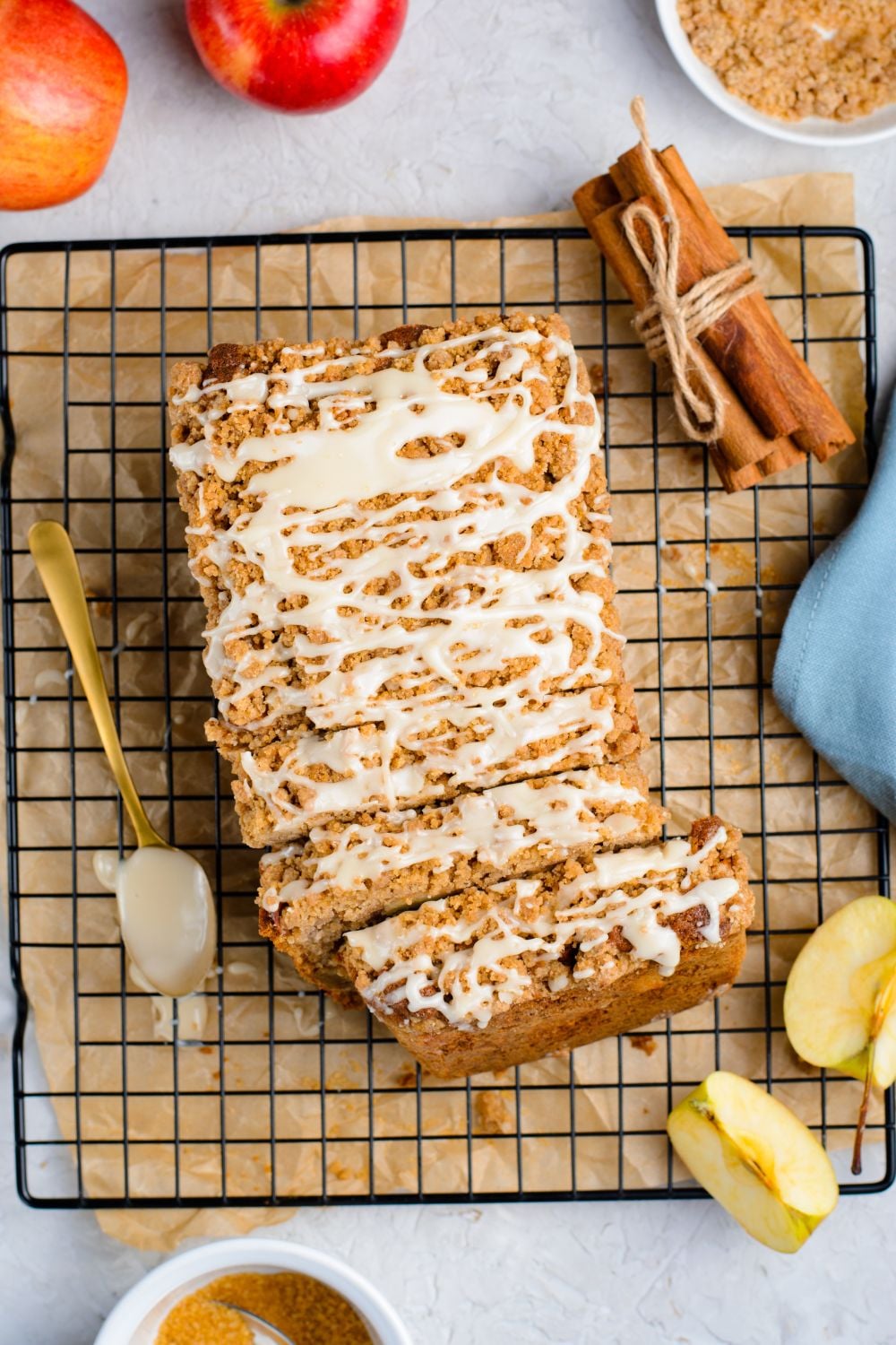 Apple Cinnamon Loaf Cake on a cooling rack on marble counter with a bundle of cinnamon sticks to the side, apples, sliced apples and more to decorate it for fall