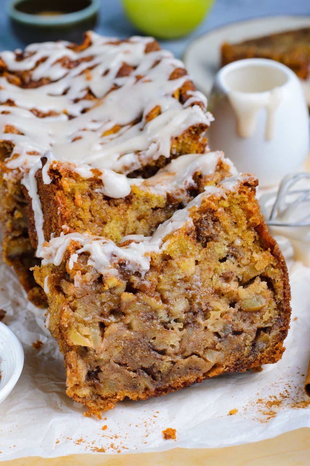 sliced Amish Apple Fritter Bread sitting on parchment paper on a wooden table with a sweet glaze drizzled on top