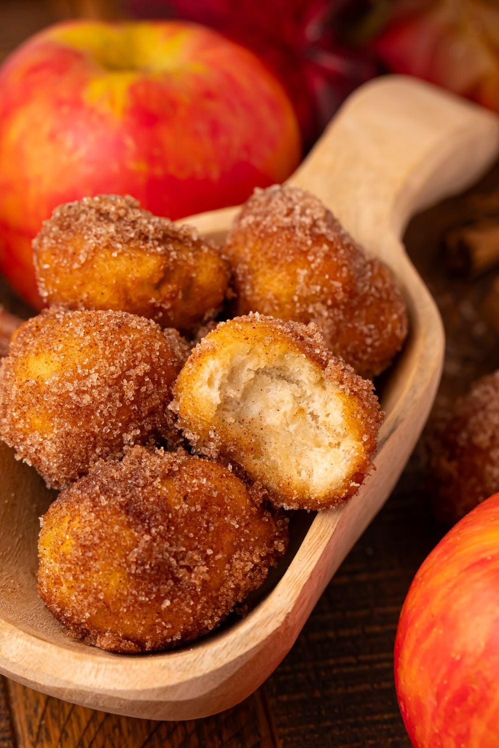 Apple Pie Donut Holes in a wooden spoon on table with some apples beside the spoon 