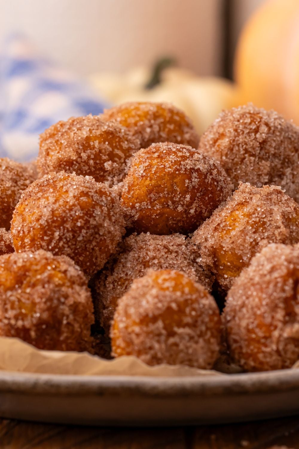 side view of Pumpkin pie donut holes in a bowl on table with a blue checkered towel in the background of picture