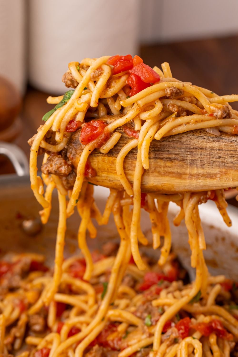 wooden tongs with a bunch of taco spaghetti being lifted out of skillet