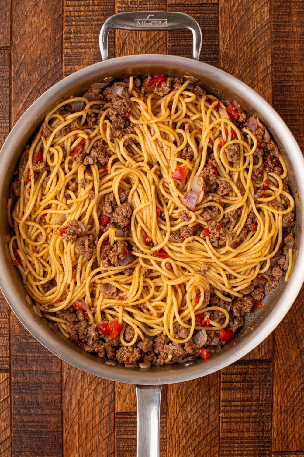 a skillet on wooden table with ground beef, veggies and pasta inside being mixed up