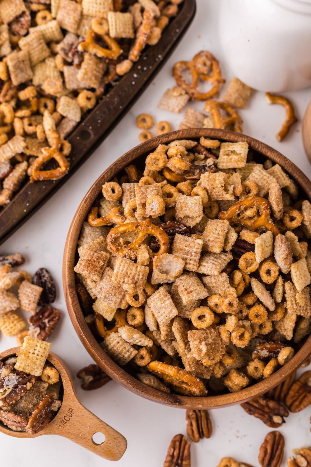 Pumpkin Spice Chex Mix in a wooden bowl and a measuring cup and sheet pan full of pumpkin snack mix