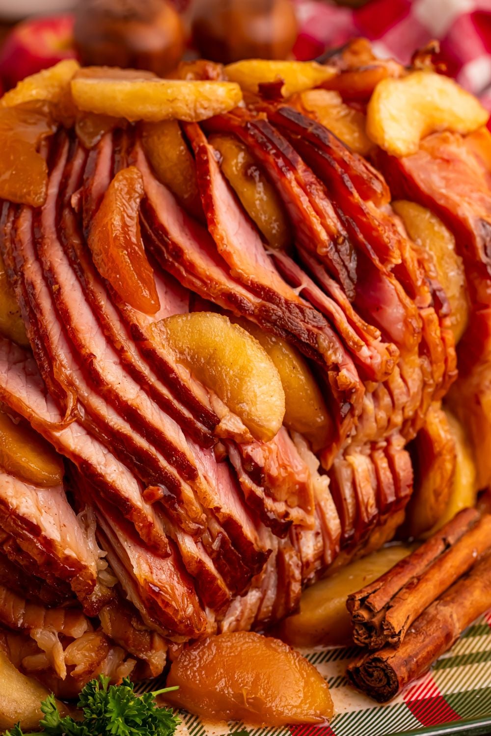 side view of a Slow Cooker Apple Glazed Ham sitting on a platter with cinnamon sticks in front 