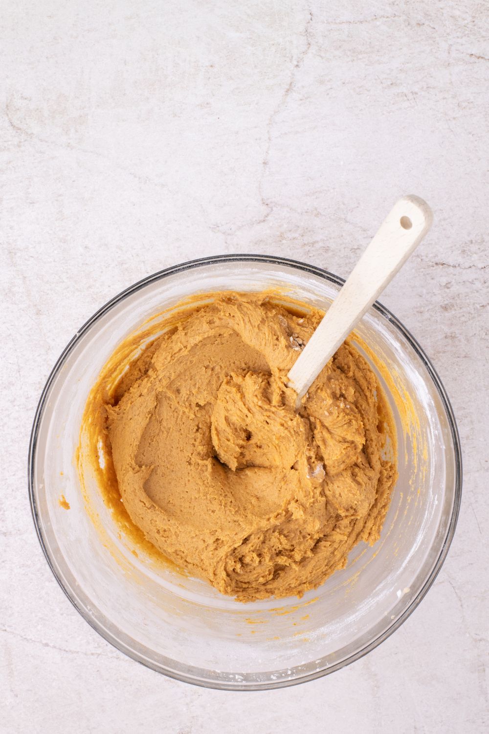 pumpkin cookie batter in a glass bowl with a spatula on table