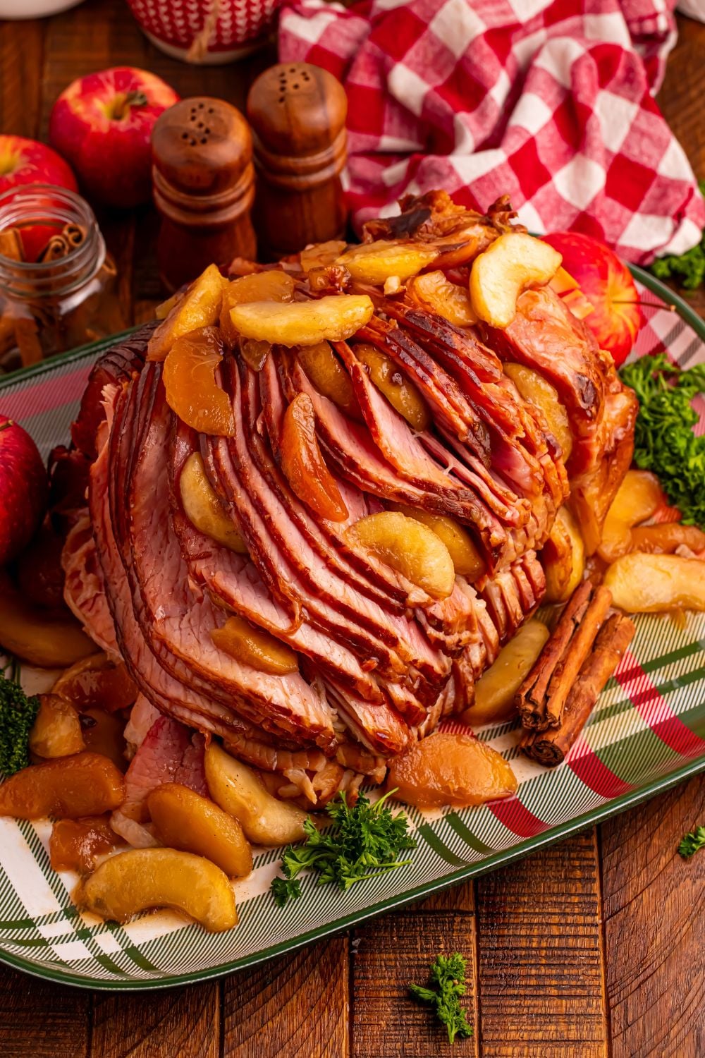 A plaid platter on a wooden table with a large Slow Cooker Apple Glazed Ham on platter, and fall themed items around it