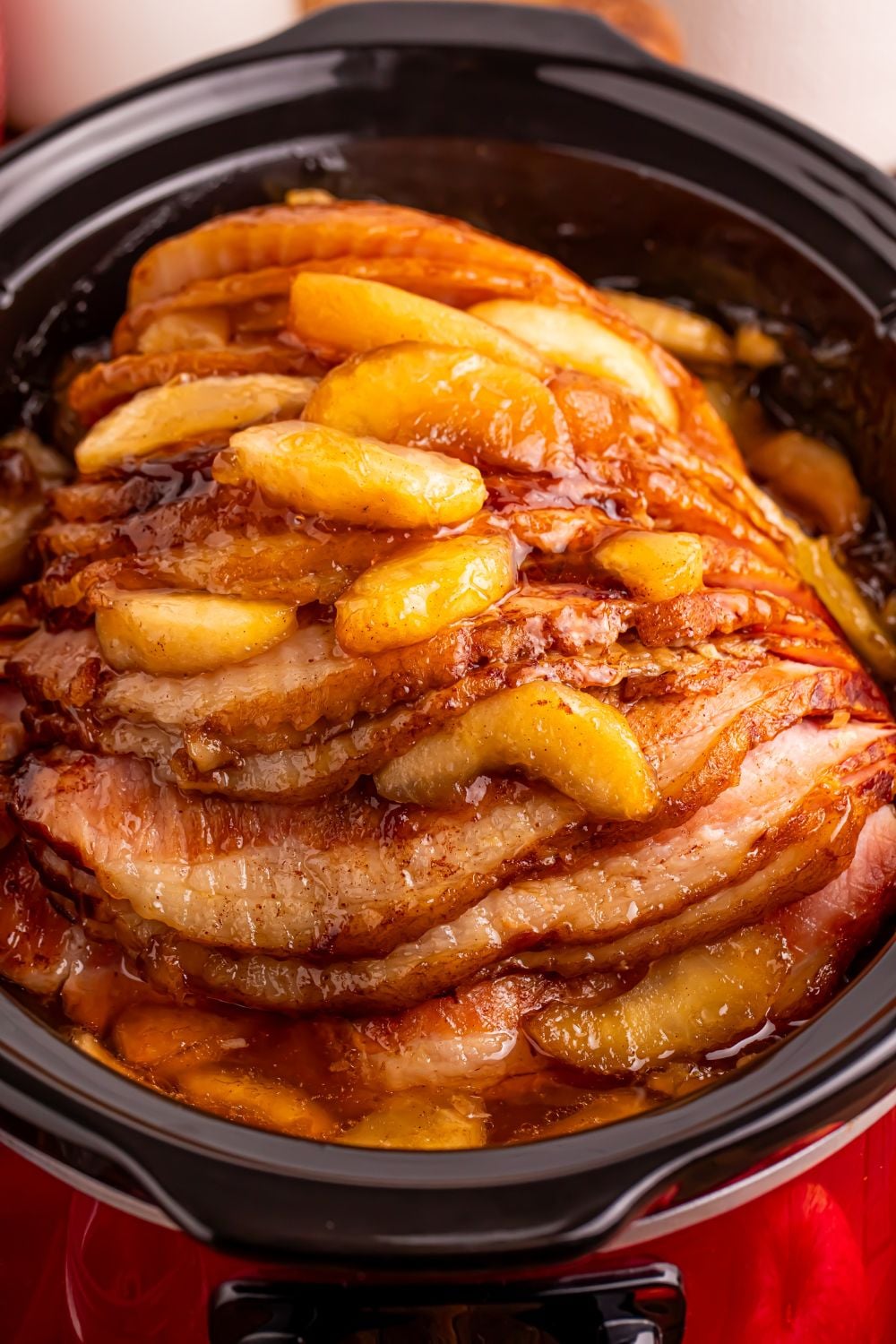 red slow cooker on table with a glazed apple spiral ham on table 