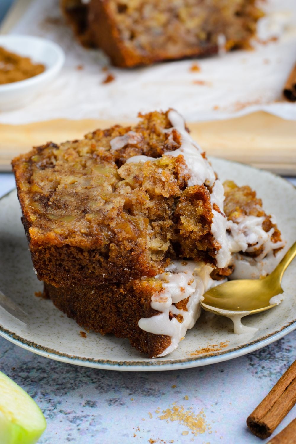 two slices of Amish Apple Fritter Bread on a white plate with a gold spoon to side showing a couple bites taken out of it