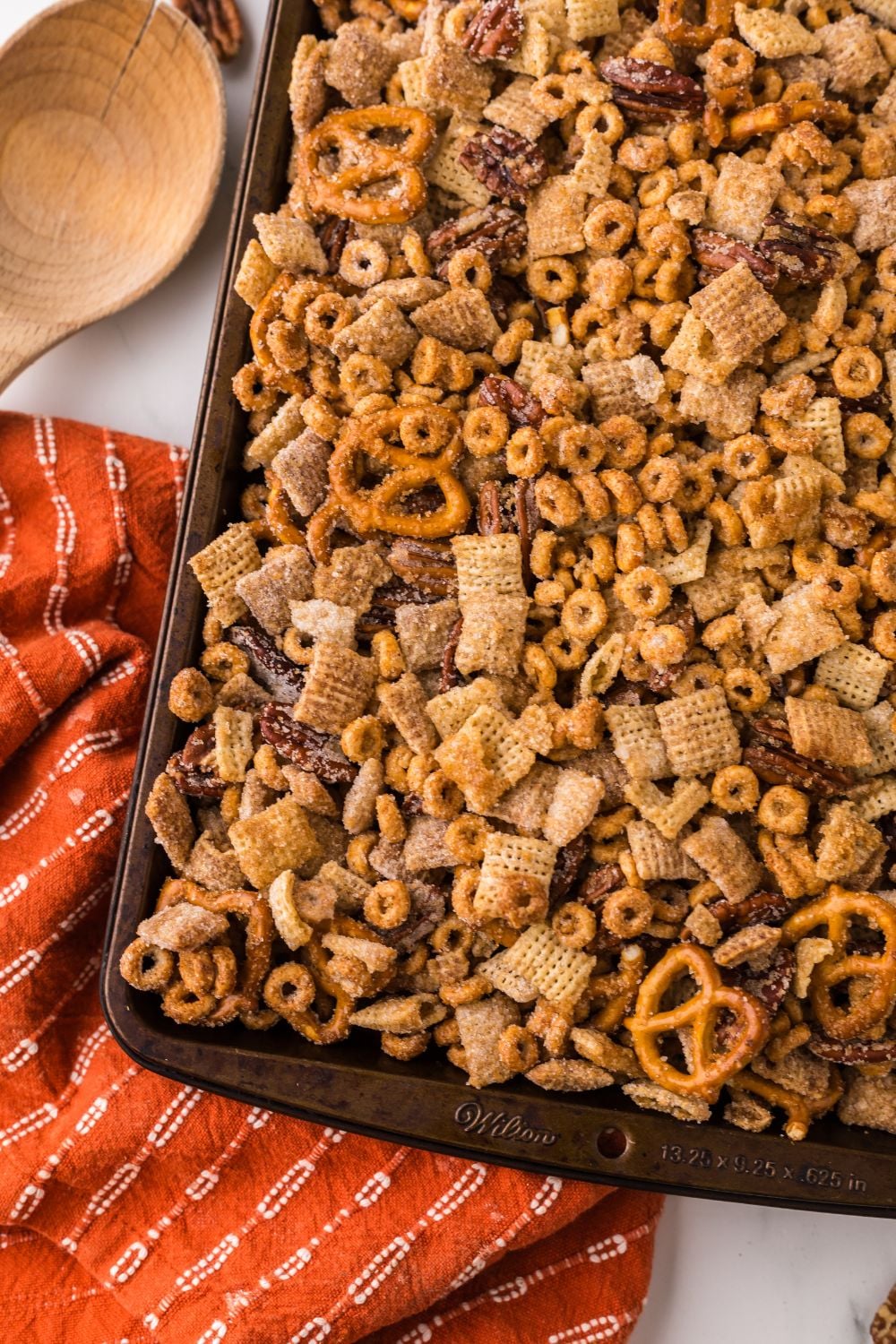 Pumpkin Spice Chex Mix spread out over a sheet pan with an orange striped towel on marble counter 