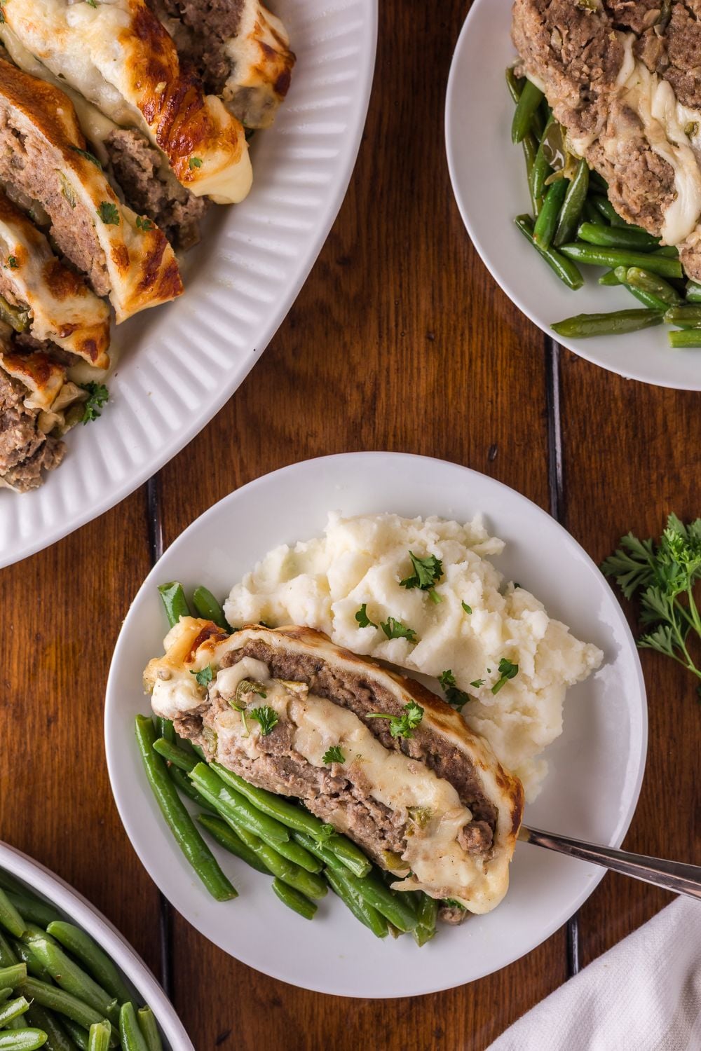a dinner table with a platter full of sliced Stuffed Philly Cheesesteak Meatloaf, and plates that have meatloaf, mashed potatoes and green beans on it