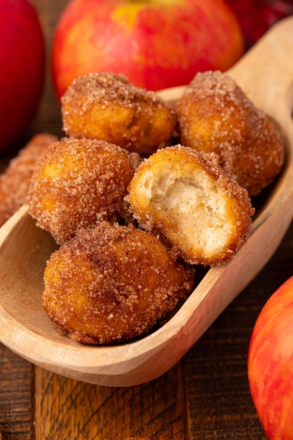 wooden spoon with a handful of Apple Pie Donut Holes sitting on a wooden table with apples around it 
