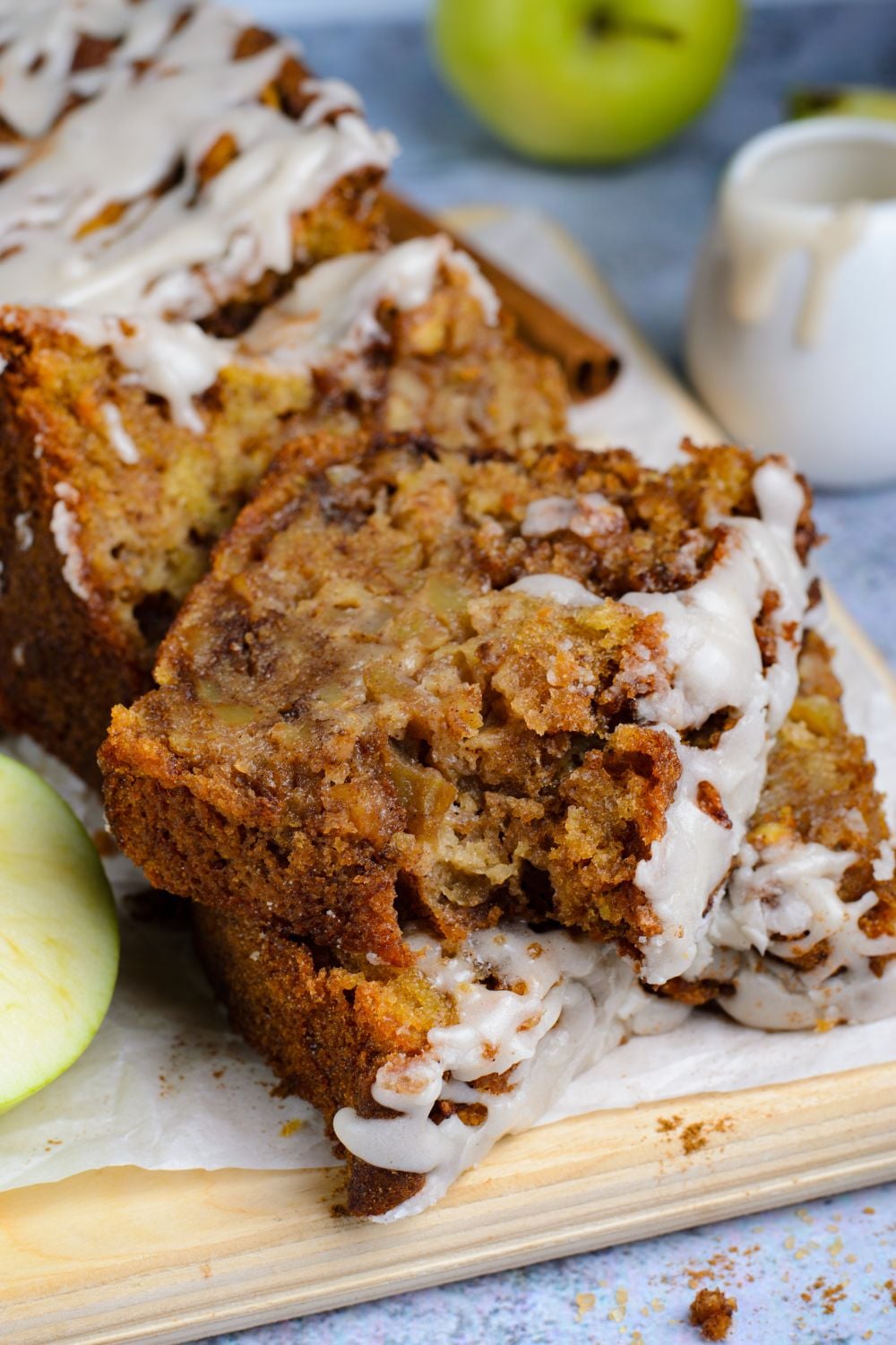 Apple bread with real apples sliced and placed on table with a bite taken out of the top slice of bread and apples around it on table for decor