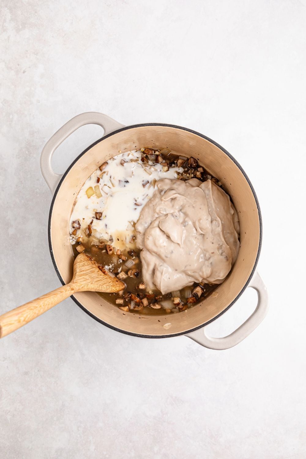 cream colored saucepan on table full of cooked veggies, cream soup and milk with wooden spoon 