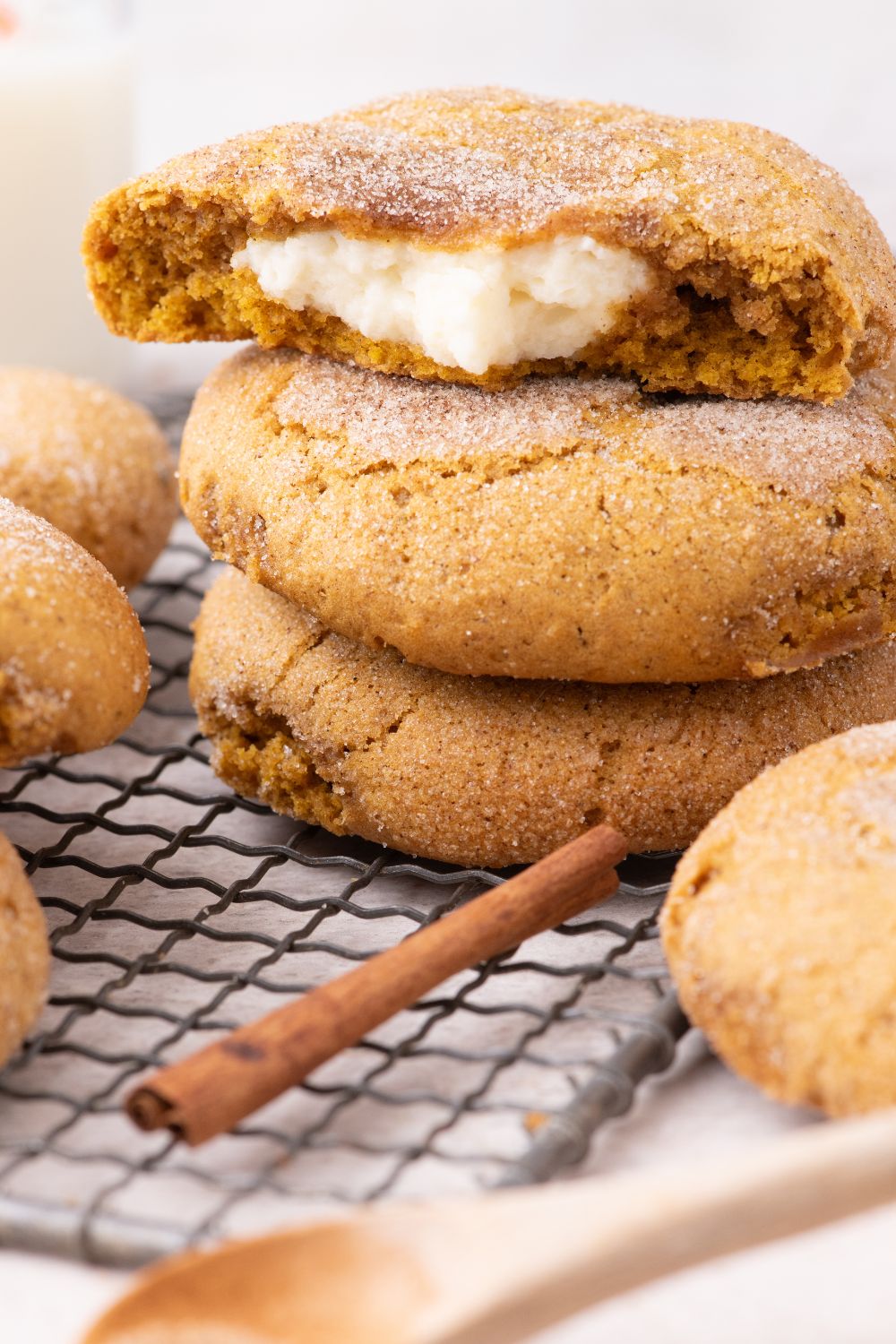 Pumpkin Cheesecake Cookies stacked on a cooling rack on table with a cinnamon stick and wooden spoon in front