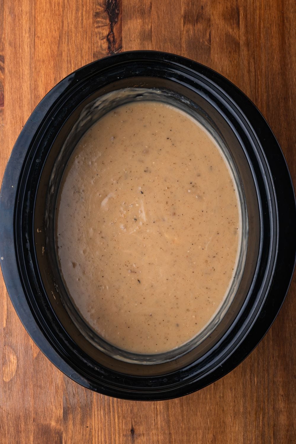 creamy Crockpot Loaded Baked Potato Soup sitting in a black crockpot sitting on a wooden table