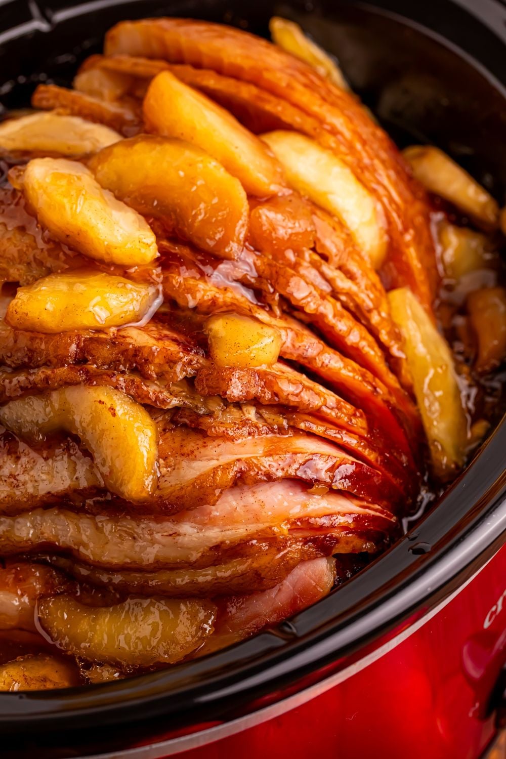close up look of a red slow cooker with a apple topped spiral ham