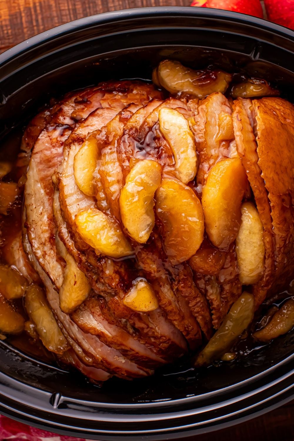 looking down at a black slow cooker with a spiral cut ham and baked apples on top of the ham
