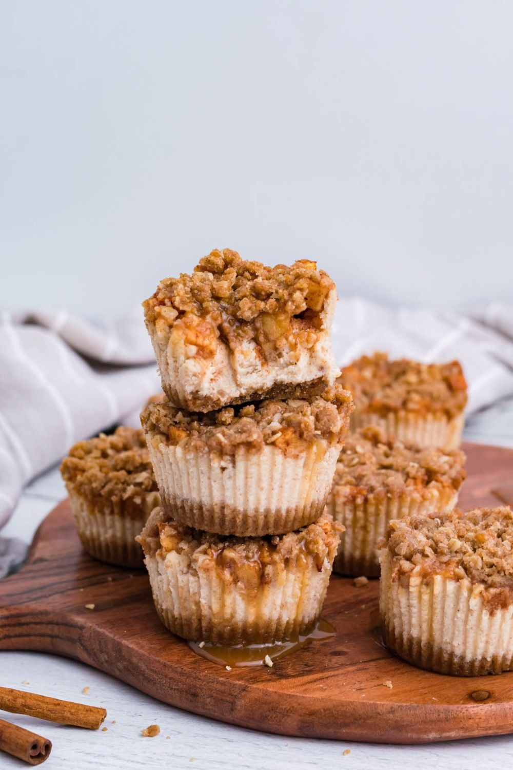 marble counter with a round cutting board on it, with stacks of Apple Crisp Cheesecake Bites. There are cinnamon sticks to side on table