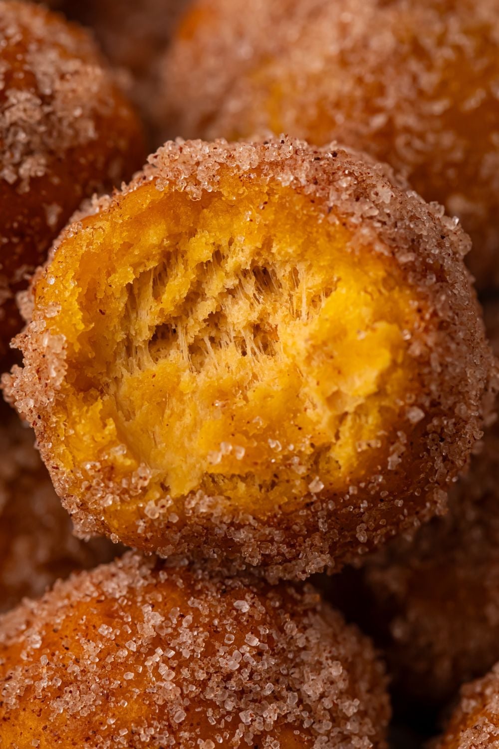 Pumpkin Pie Donut Hole with a bite taken out of it, sitting on a pile of more of the donut holes