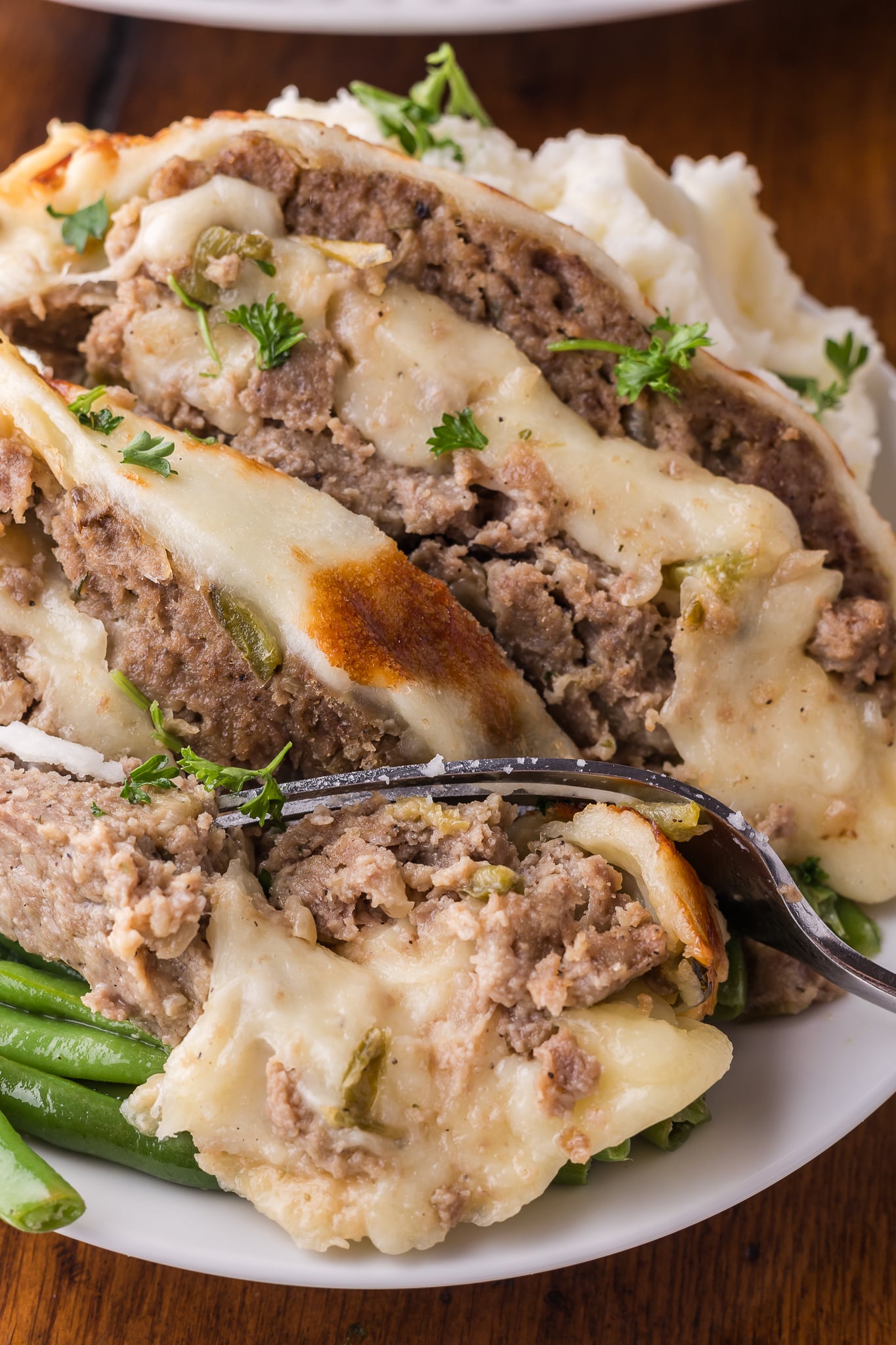 Up close shot of the Philly Cheesesteak Meatloaf sliced on a white serving plate with a fork taking out a bite