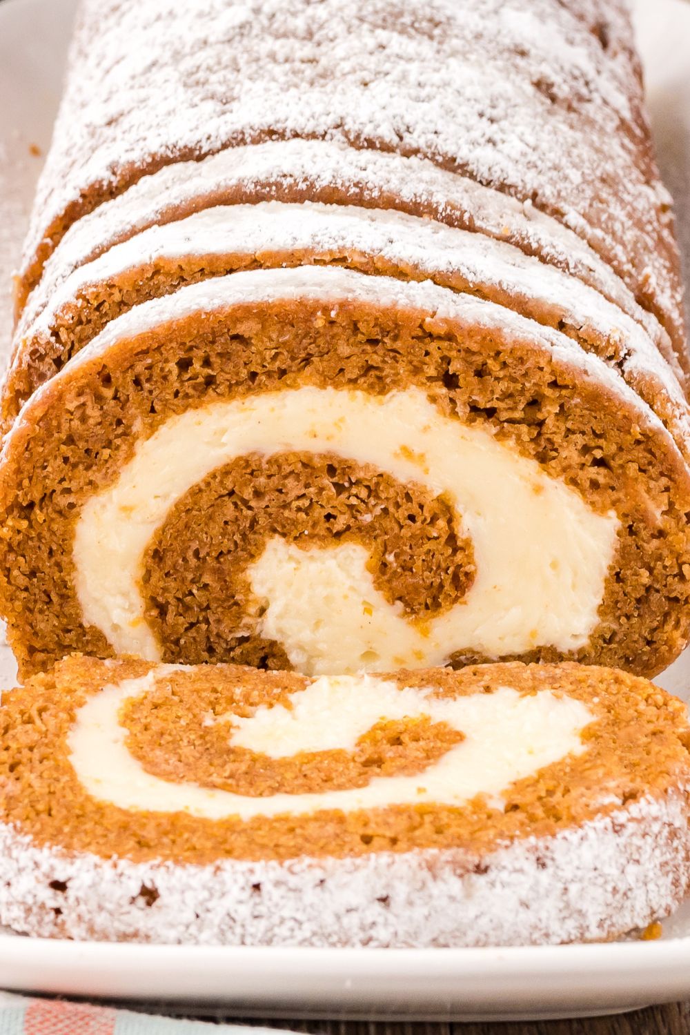close up of Pumpkin Cake Roll on a platter so you can see the swirl of filling in the pumpkin roll