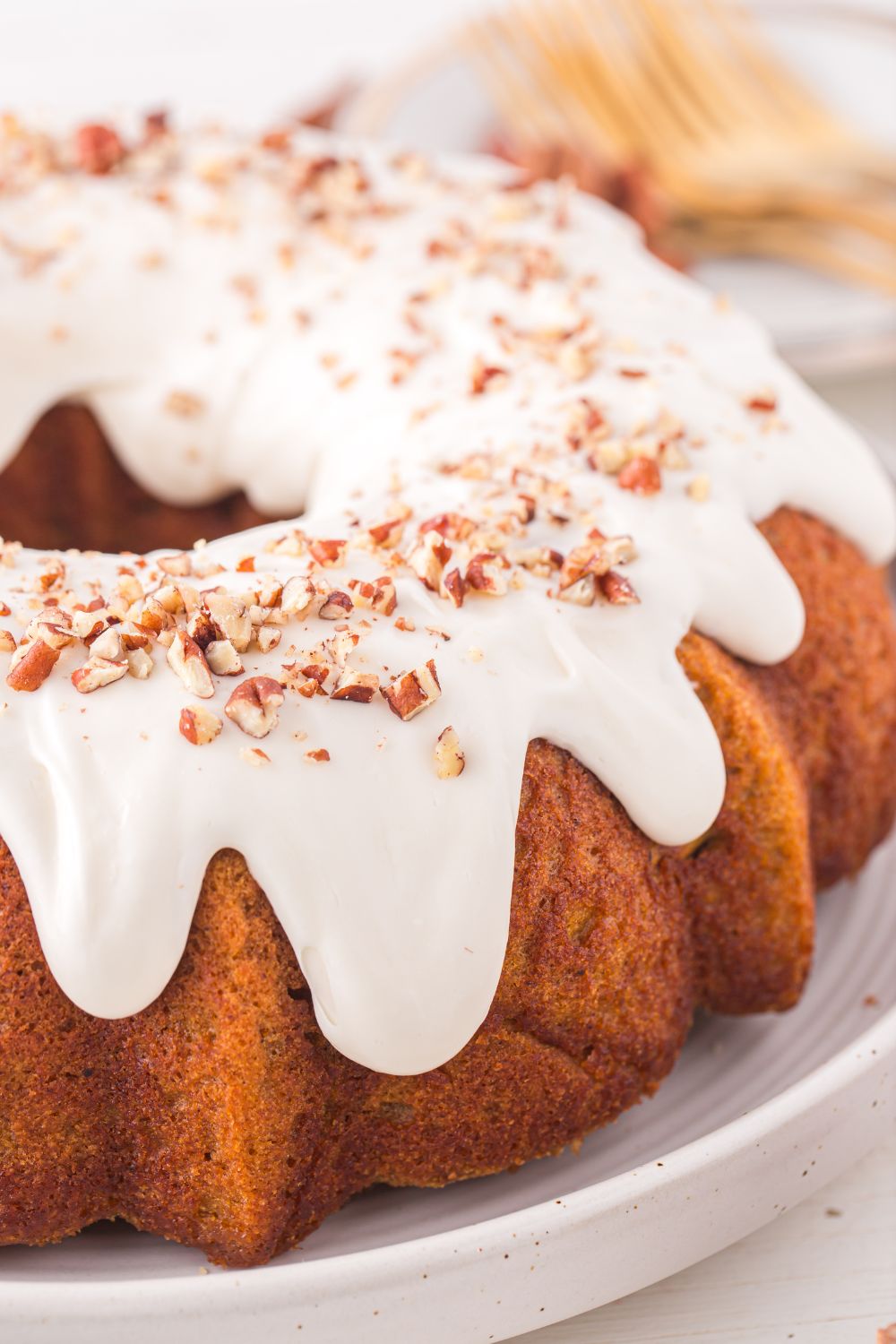 Pumpkin Bundt Cake on a white platter that is topped with cream cheese glaze and chopped nuts