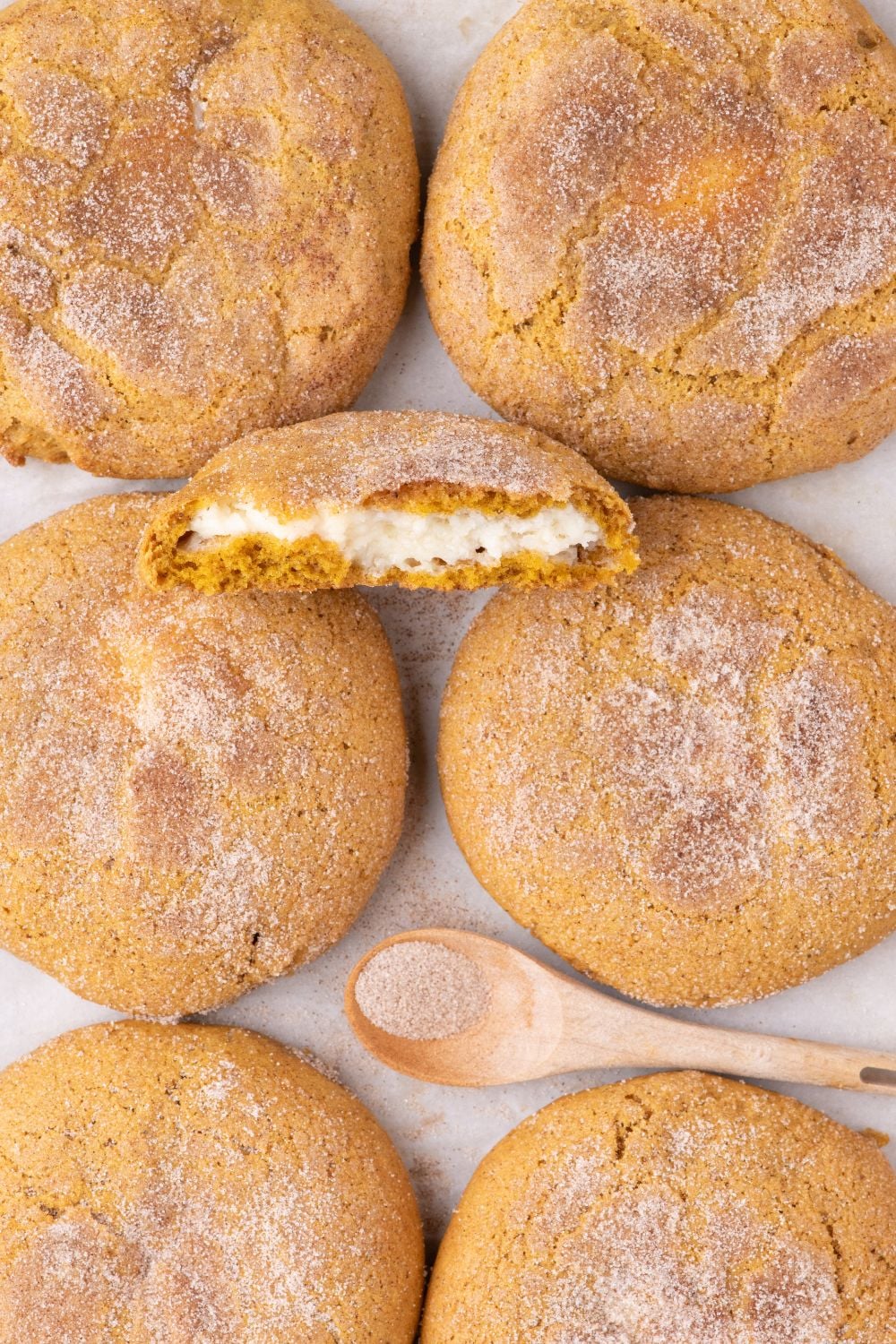Pumpkin Cheesecake Cookies placed on table with one cookie cut in half and a spoon of cinnamon and sugar