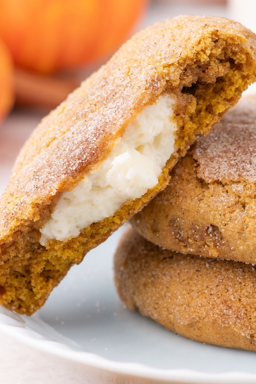 2 Pumpkin Cheesecake Cookies on a white plate with one cookie with some bites out of it to show the cheesecake filling