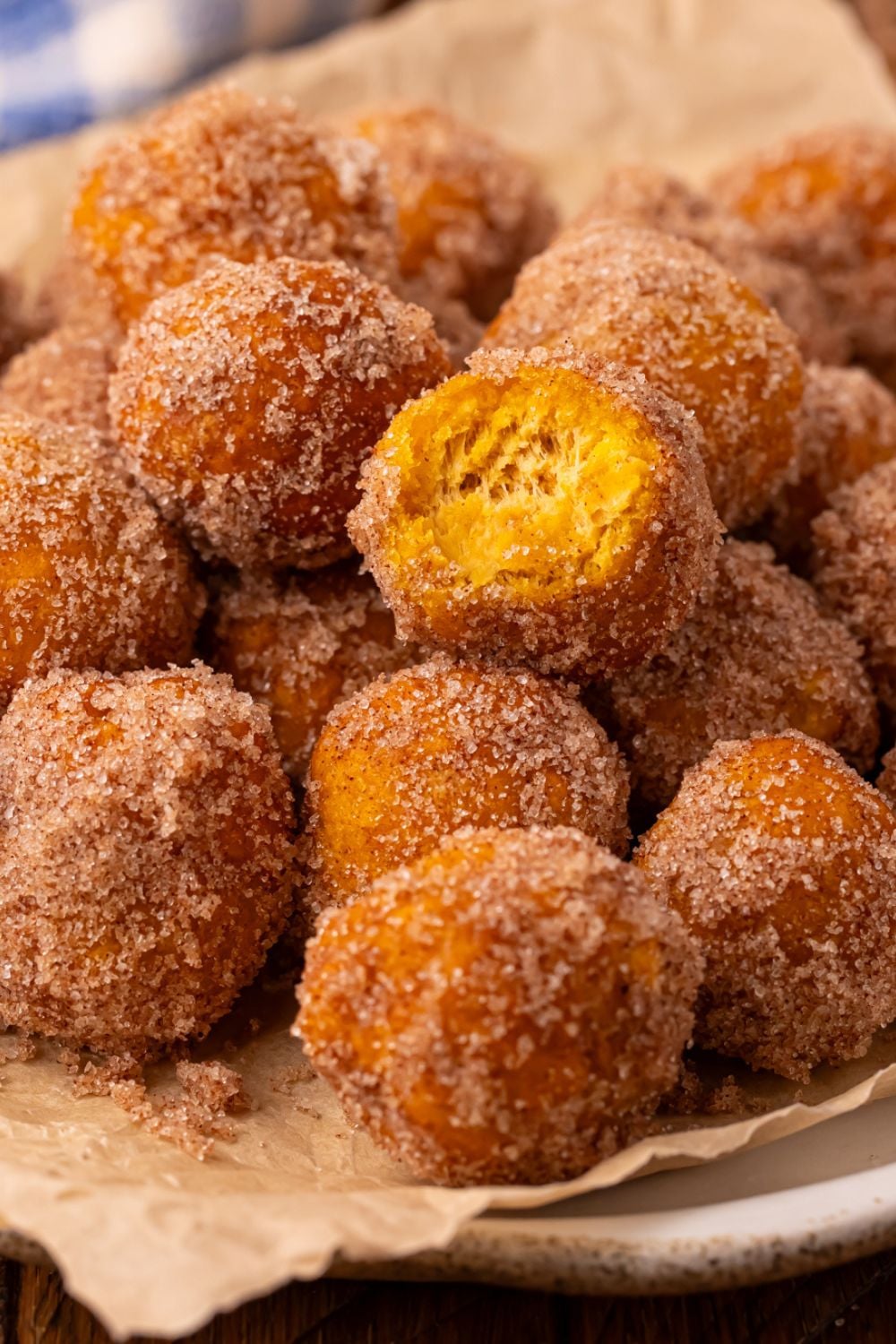 donut holes rolled in cinnamon and sugar on a platter with one donut bit in half to show how fluffy it is