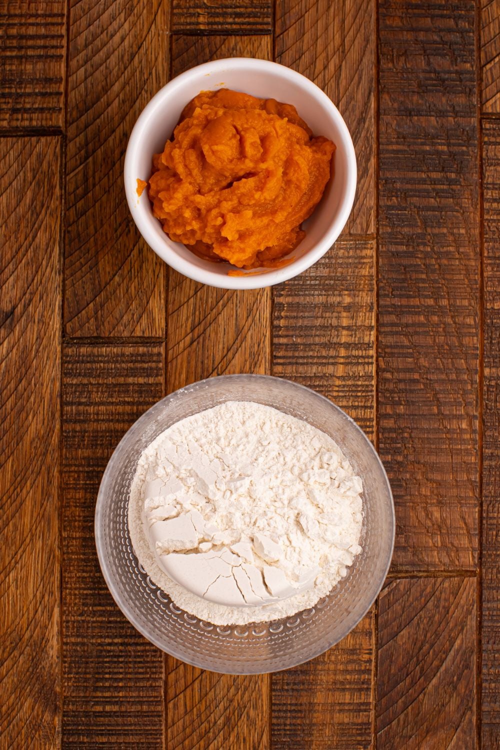 self rising flour in a glass bowl and a bowl of pumpkin puree in a white bowl on wooden table