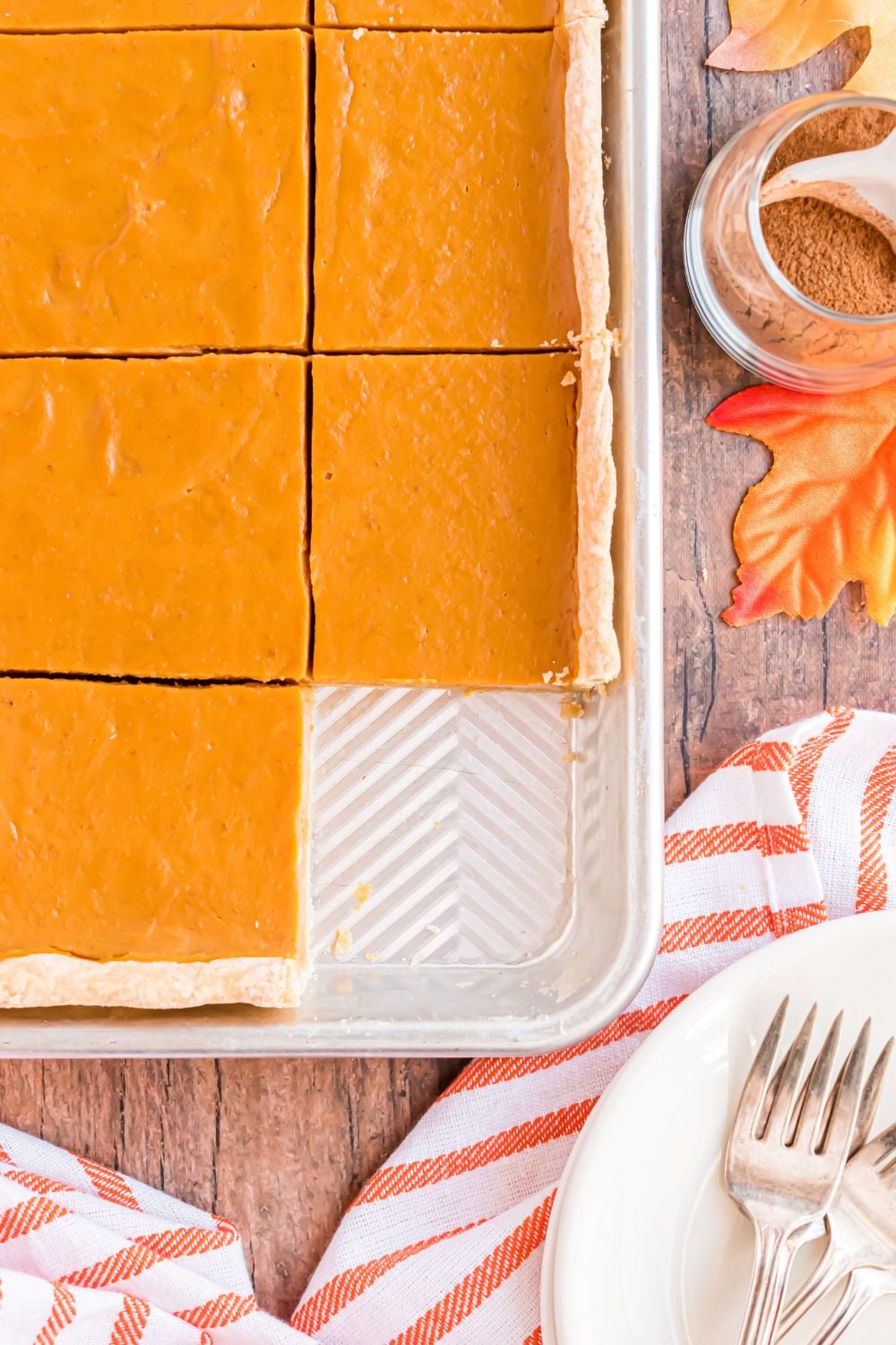 rustic wooden table with fall decorations and a Sheet Pan Pumpkin Pie with one slice removed from the pan, with a white plate and fork sitting in front of the sheet pan. 
