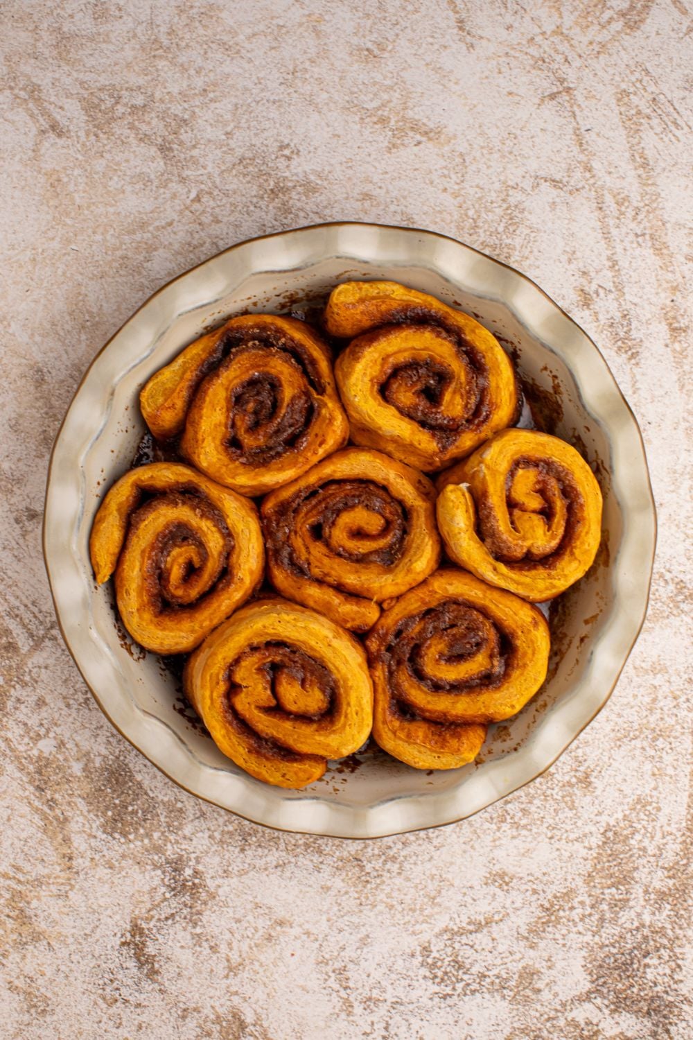 baked Pumpkin Cinnamon Rolls in a pie plate sitting on counter 