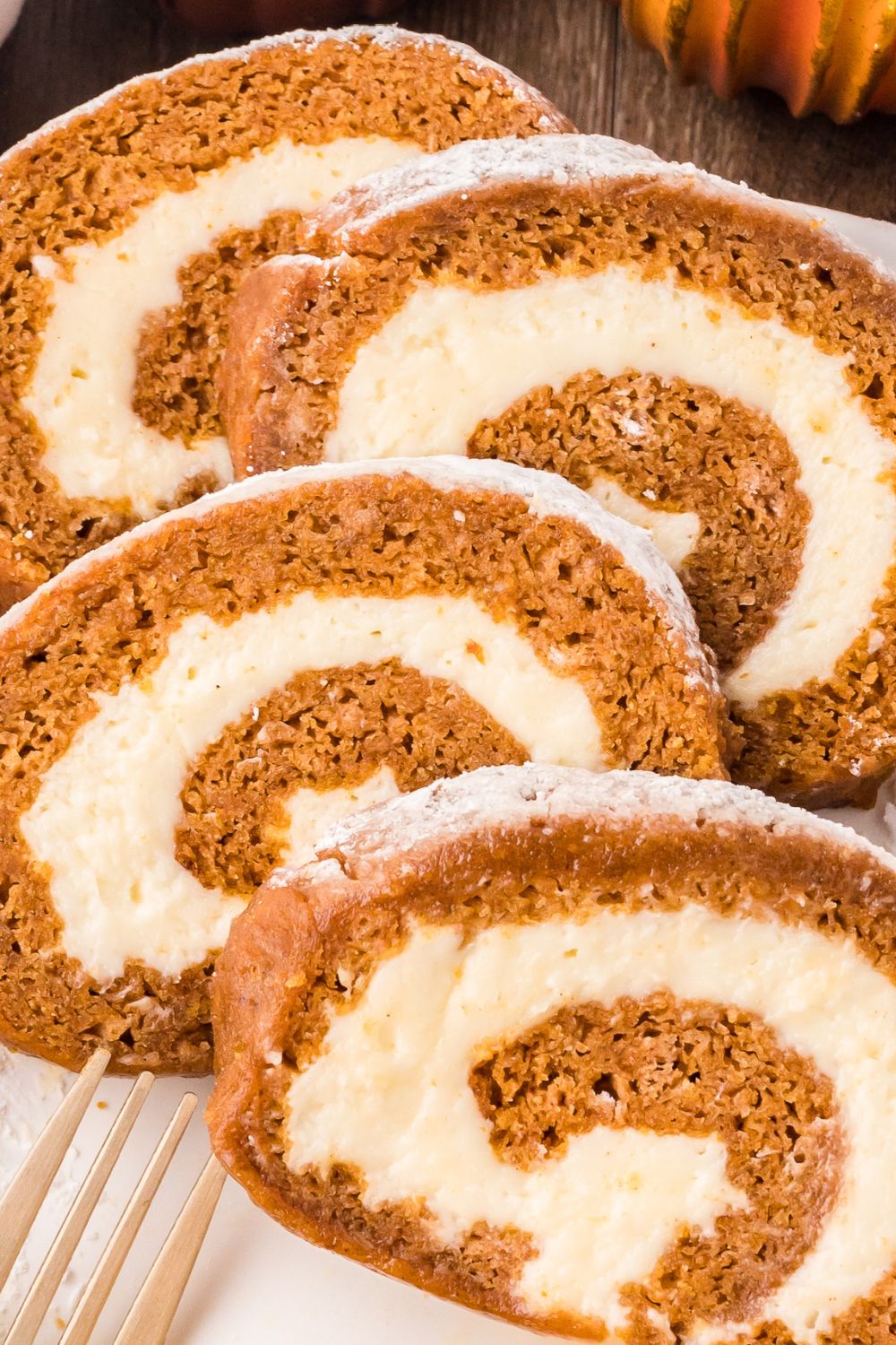 thick slices of Pumpkin Cake Roll on a white plate with a fork sitting in front of the plate that is sitting on a wooden table