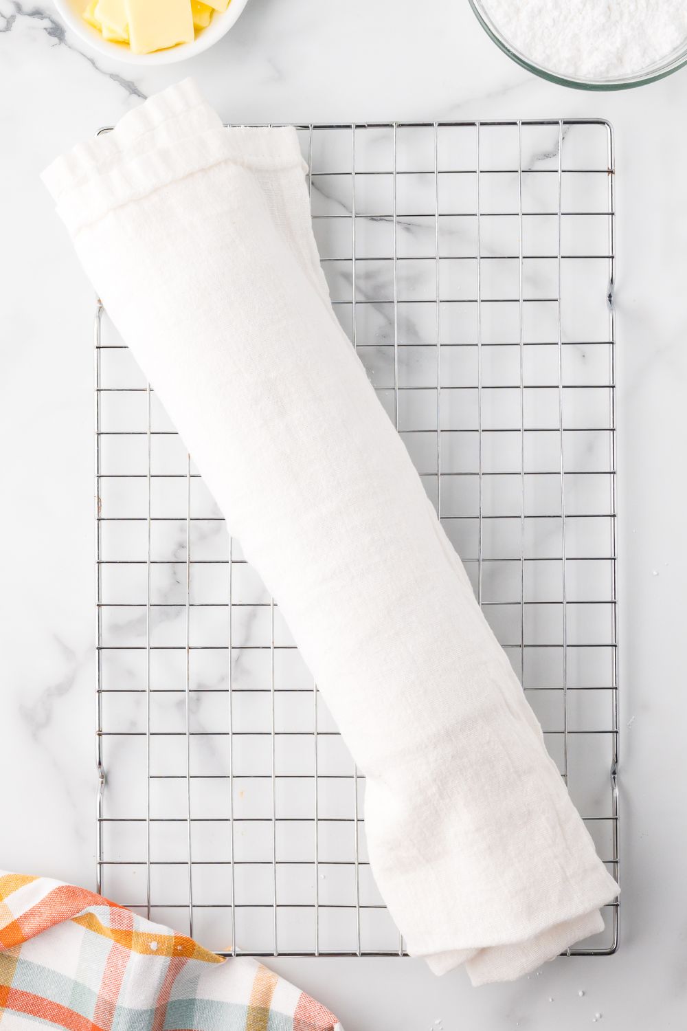 Pumpkin Cake Roll wrapped up in a white towel on a cooling rack on a marble counter