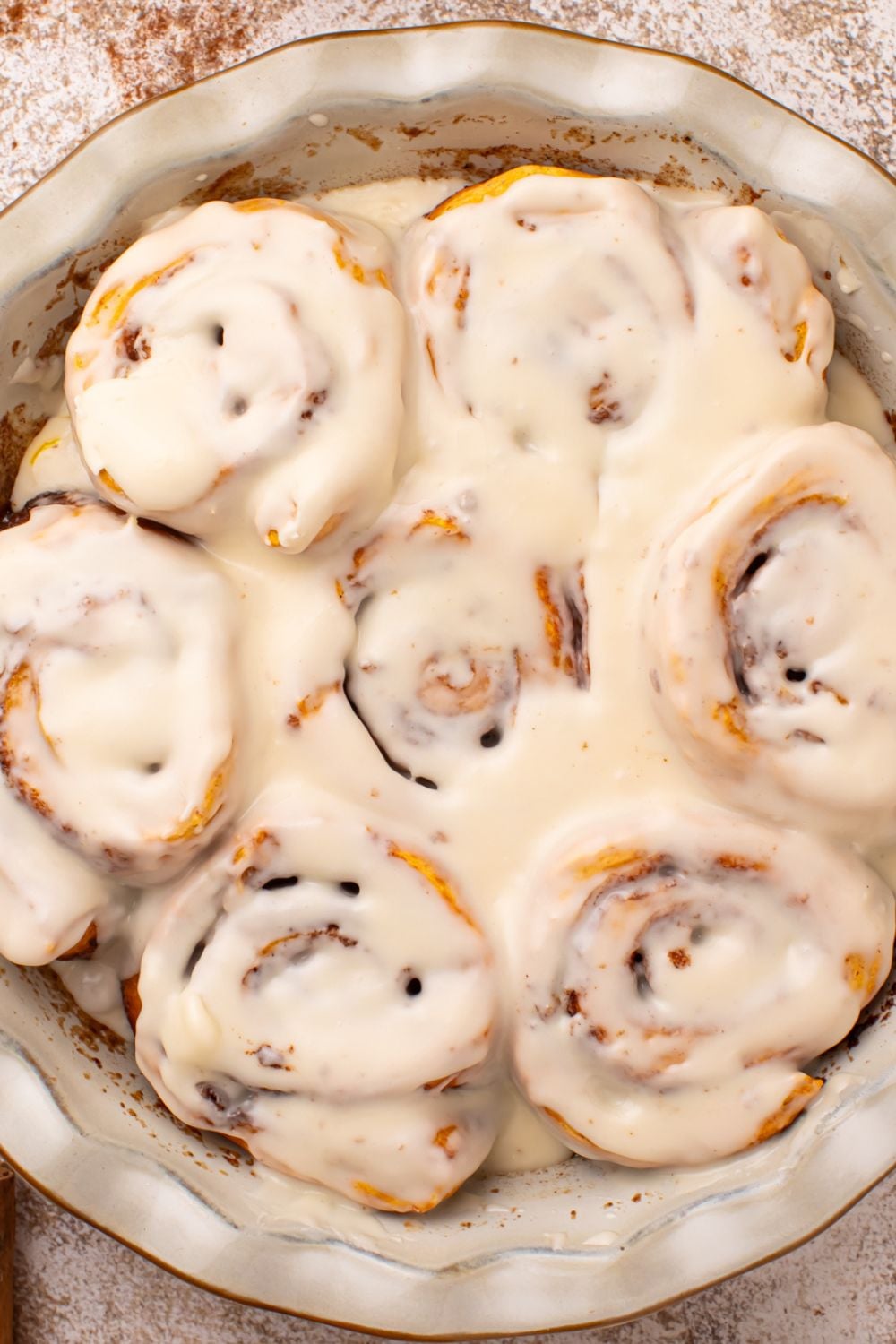 looking down at table to a round pie plate full of baked and glazed Pumpkin Cinnamon Rolls on the table 
