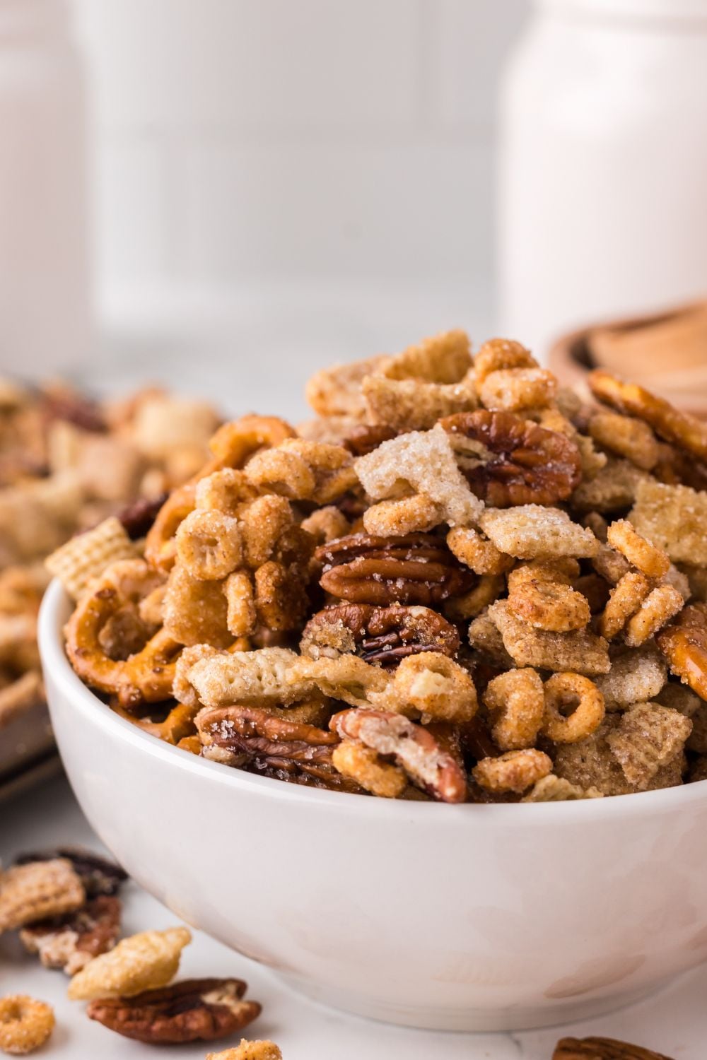 Pumpkin Spice Chex Mix scattered around on table and overflowing in a white bowl sitting on a marble counter